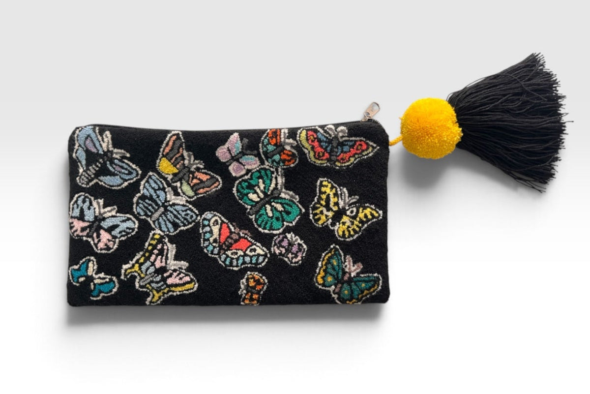 By M. Design A black zippered pouch decorated with colorful embroidered butterflies, featuring a black tassel with a bright yellow pom-pom on a light gray background.
