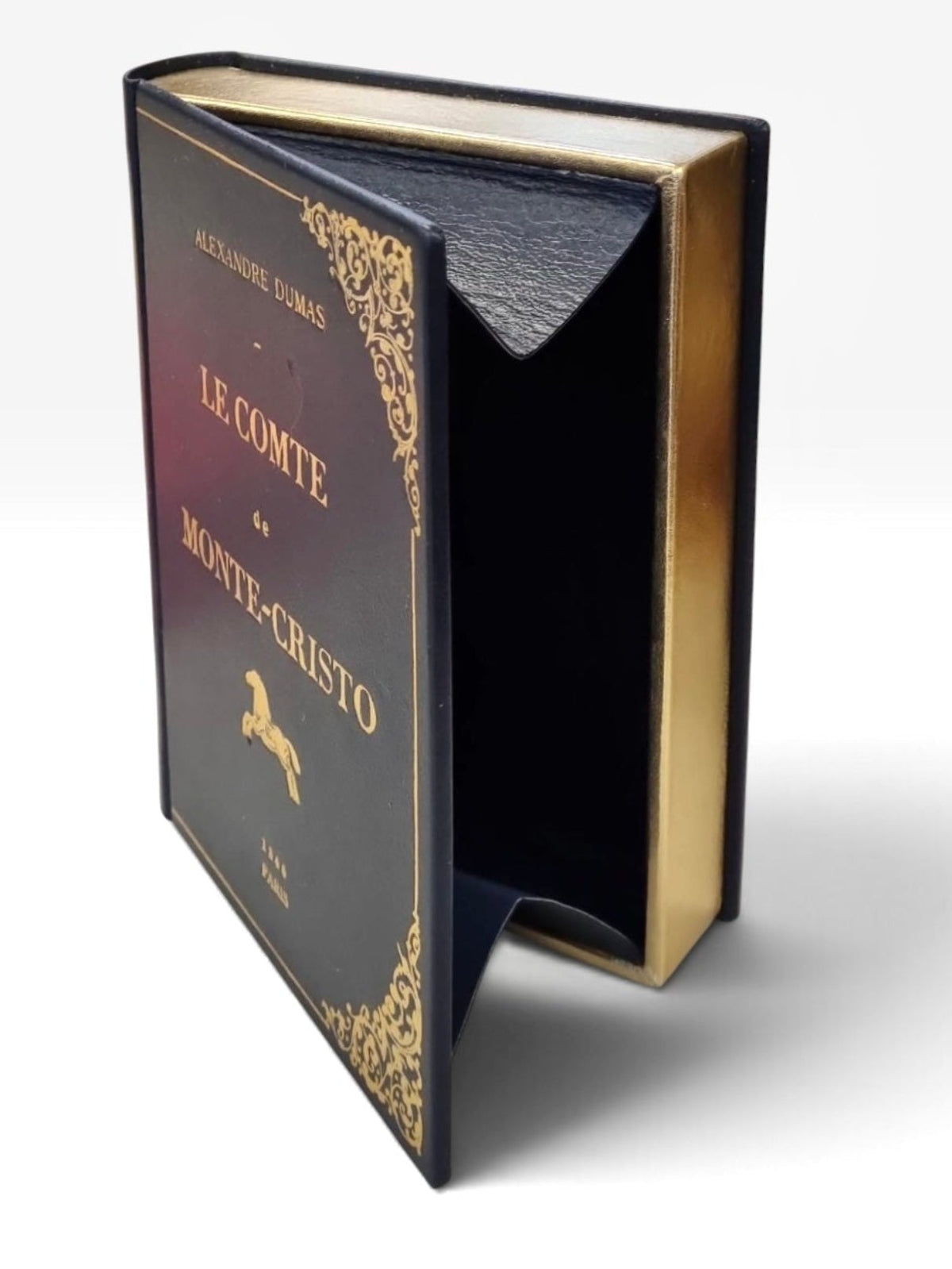 A vintage-style book-clutch by maria marigliano caracciolo set with a dark navy blue cover, gold decorative borders, and gold lettering, shown open to reveal a dark interior lined with matching navy velvet. le compte de monte-cristo. 