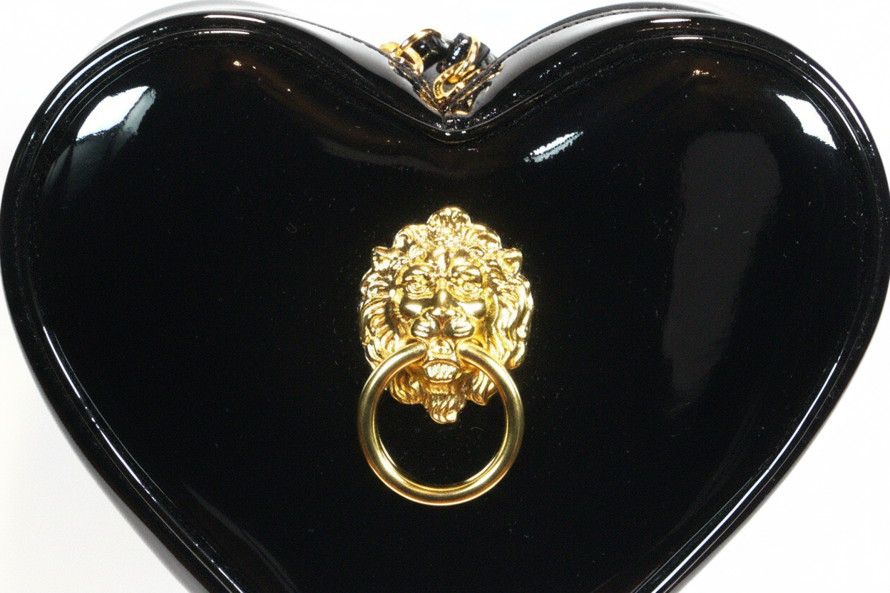 Black heart-shaped bag with gold lion head design on a white background