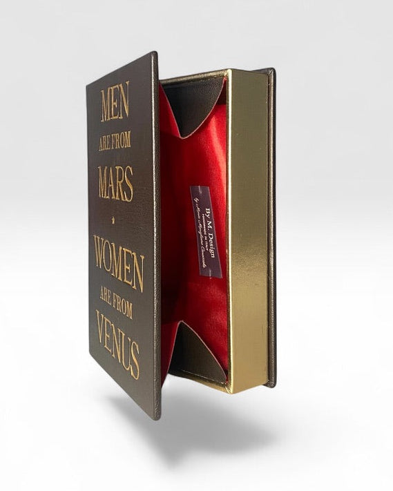 book-clutch bag titled 'Men and From Mars and Women Are from Venus' shown floating open at an angle, in leather designed by Maria Marigliano Caracciolo