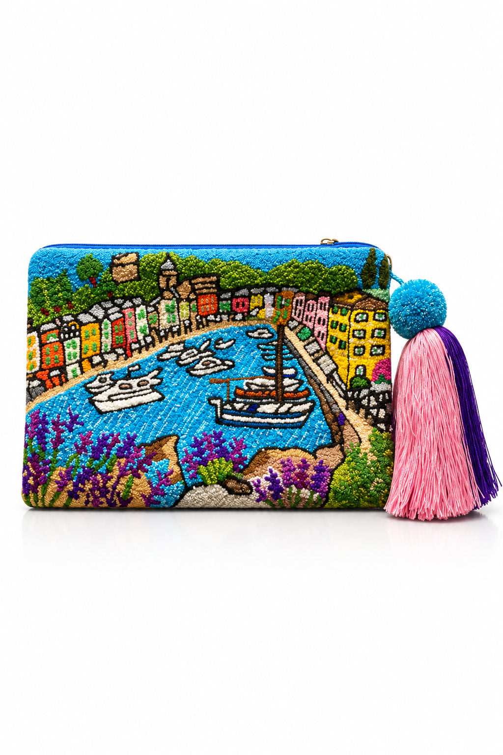 portofino clutch by maria marigliano caracciolo by m design. A rectangular embroidered clutch purse featuring a colorful coastal harbor scene with boats, buildings, and purple flowers. The clutch has a top zipper and is adorned with a decorative tassel on the right side, featuring a blue pom-pom and pink and purple threads, set against a light gray background.